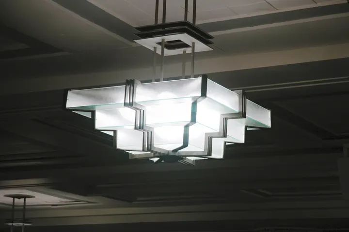 A glowing ceiling fixture with layered rectangular glass and metal shapes.