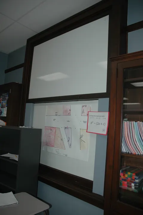 A tall framed classroom board above a bulletin area and beside a bookshelf.