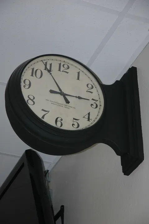 A round school clock on a bracket projecting from a wall.