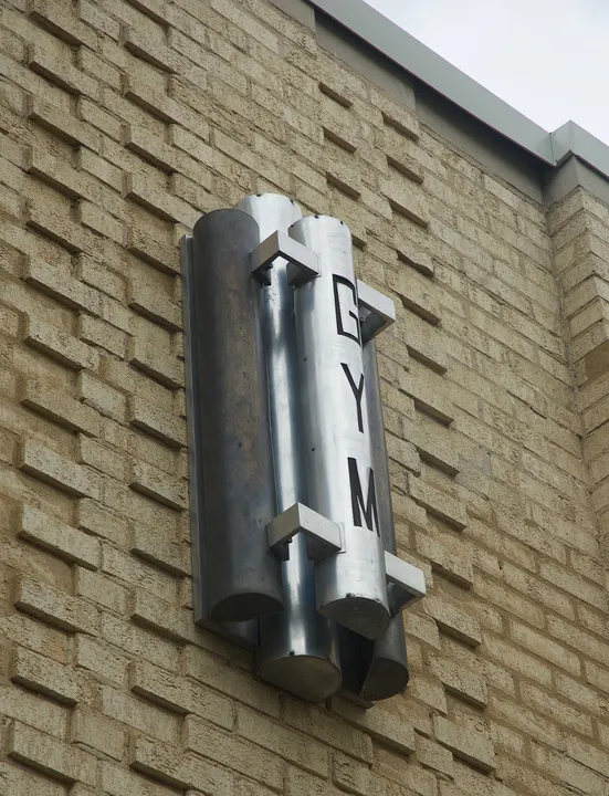 A geometric metal light with vertical GYM lettering mounted on a brick wall.