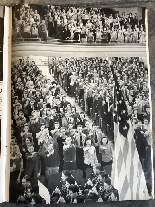 Students in a crowded school assembly taking part in a historical flag-pledge ceremony.
