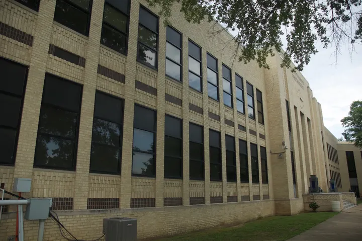 Rows of dark-framed windows set in a pale brick school facade.