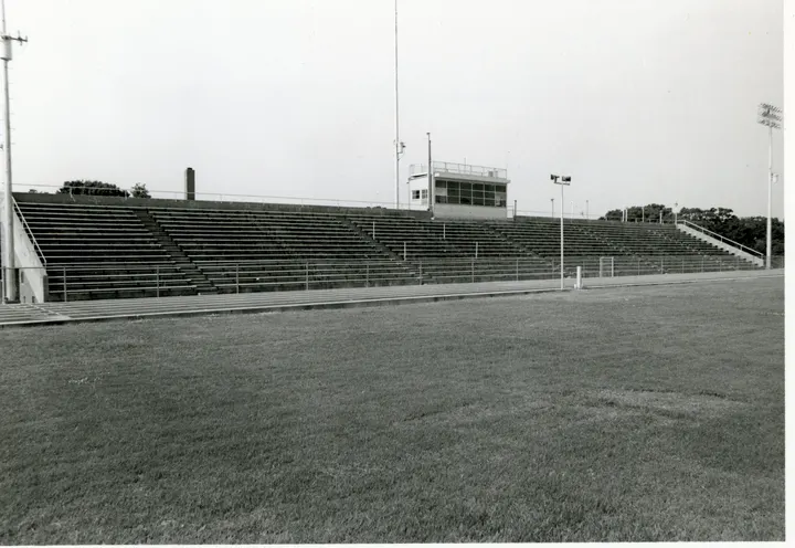 A football field facing stadium bleachers, a press box and a tall light tower.