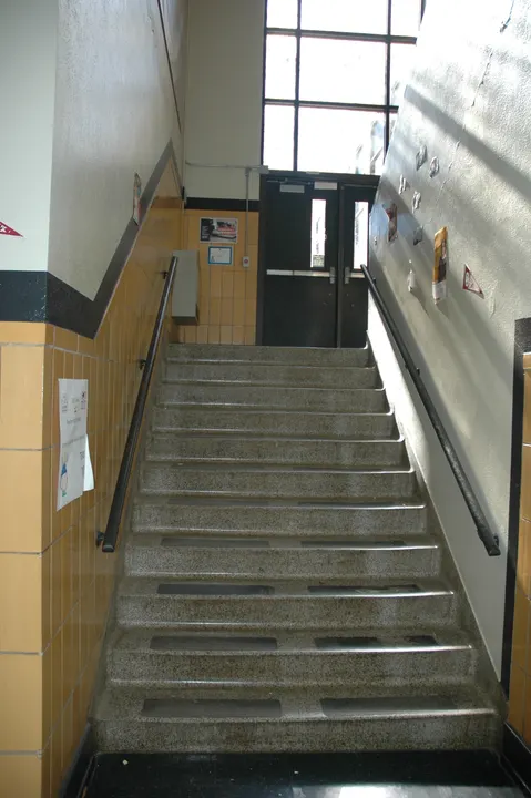An interior flight of stairs leading toward a tall window and doorway.