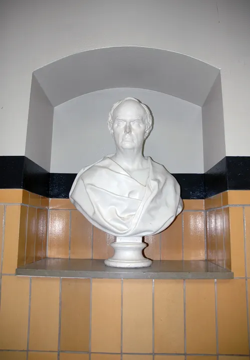 A white bust of Daniel Webster in an arched niche above warm-colored wall tiles.